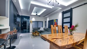 A modern dining area with a wooden table and chairs, a grey sofa, and a ceiling fan. - Sun-Soaked Paradisiac Escape|3BR, Private Beach, Pool (Plantation Village)