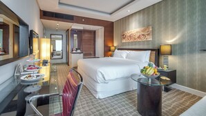 A modern hotel room with a large bed, a glass table with a fruit bowl, a mirror, and a wall-mounted artwork. - Majestic Premier Hotel Bur Dubai (Dubai)