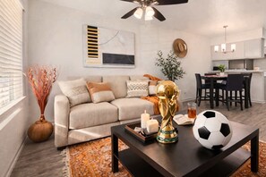 Un salon moderne avec un canapé, une table basse sur laquelle repose un ballon de football, des bougies et une statue décorative en or.