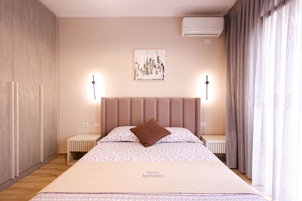 Ein Schlafzimmer mit Bett, Nachttischen, einem Kopfteil, einer Wand-Klimaanlage und einem Fenster mit Vorhängen.