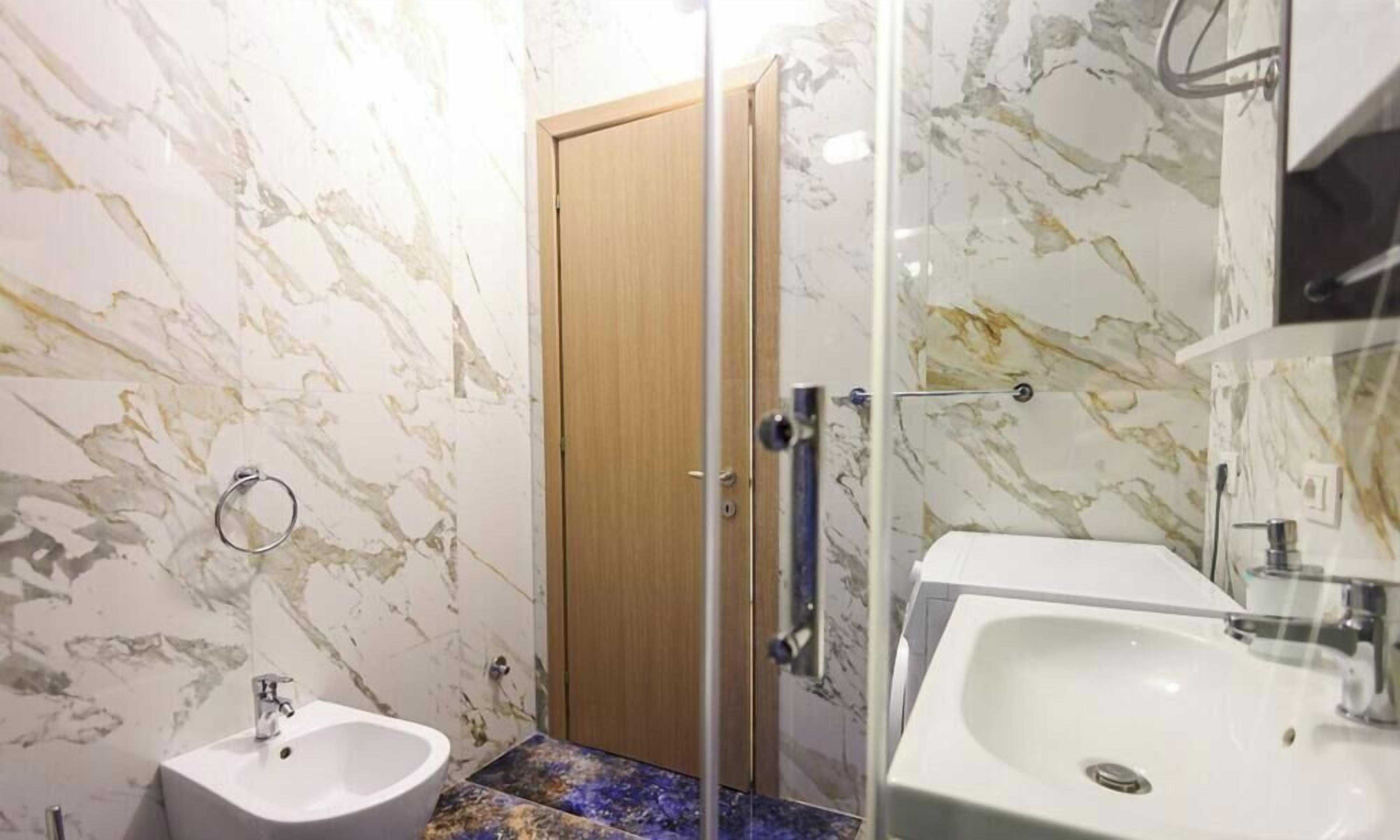 A bathroom with marble walls, a wooden door, a bidet, and a sink.