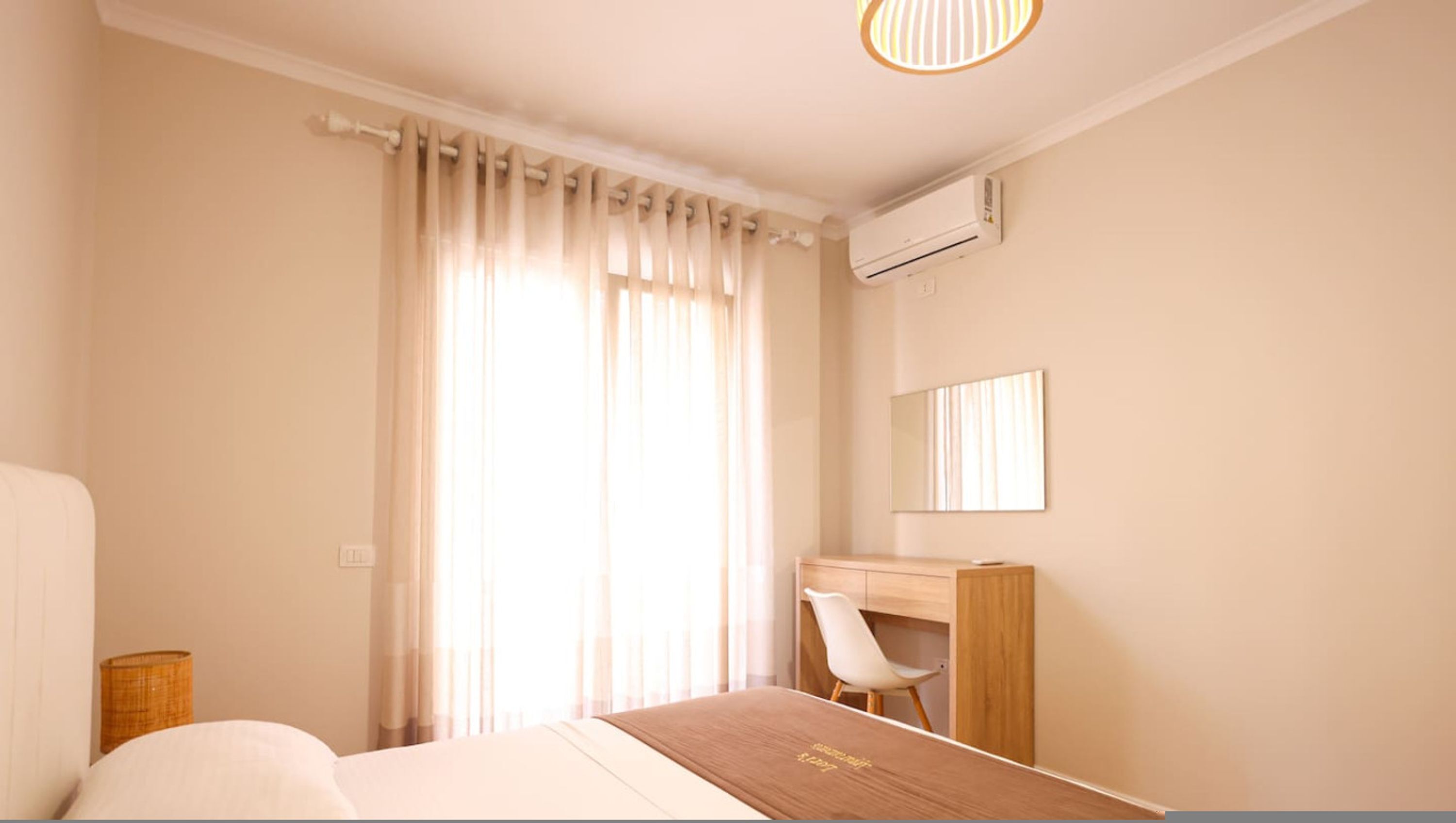 Ein Hotelzimmer mit Bett, Schreibtisch, Stuhl, einem Fenster mit Vorhängen und einer Klimaanlage.