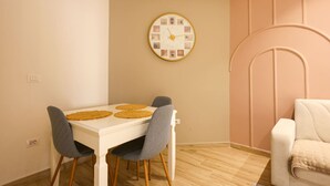 Un comedor con una mesa blanca, cuatro sillas, un reloj de pared redondo y una butaca tapizada de rosa.