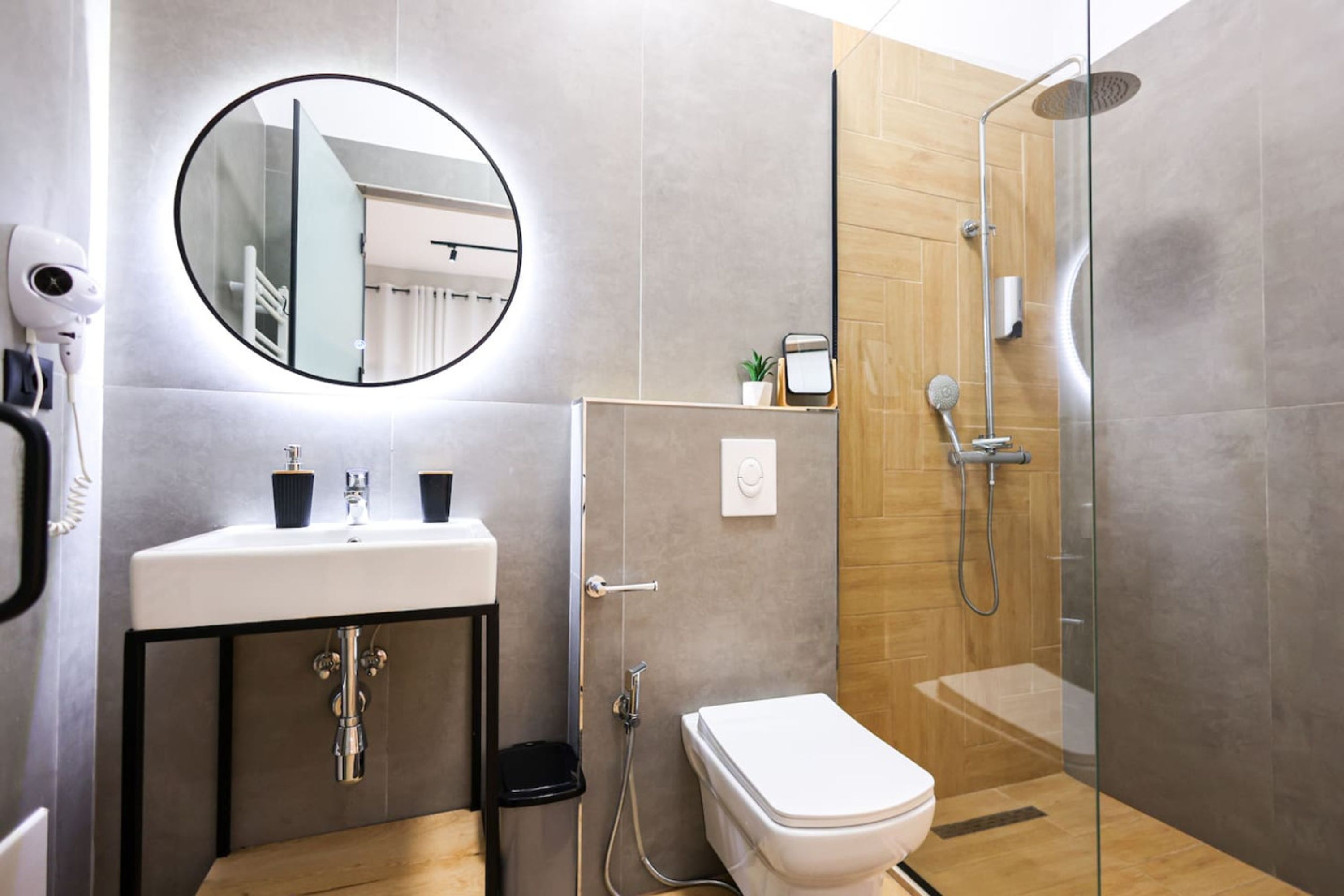 Un baño moderno con un espejo redondo, un lavamanos, un inodoro y una ducha con mampara de vidrio.