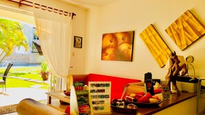 A hotel reception area with a red sofa, a coffee machine, a fruit bowl, and a wall with framed artwork. - Camera superior standard (Playa del Carmen)