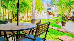 A patio area with a round table and chairs, surrounded by palm trees and a white building in the background. - Camera superior standard (Playa del Carmen)