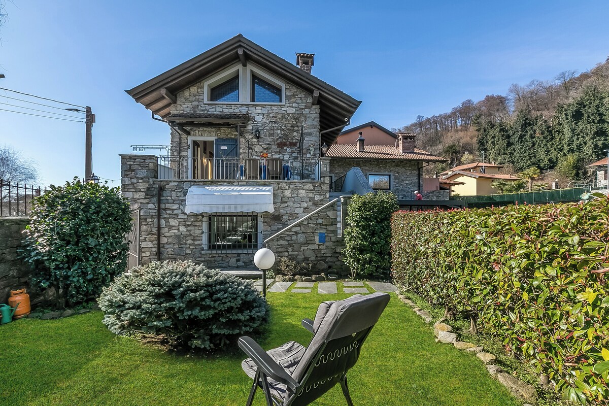 A stone house with a balcony, a lawn, and a chair.