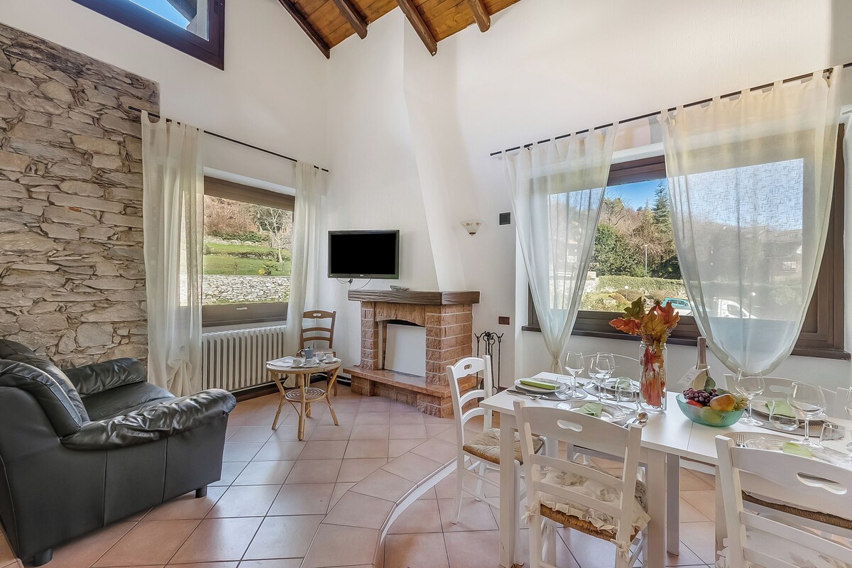 A living room with a stone wall, a fireplace, a TV, and a dining area with a table set for two.