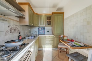 A kitchen with a stove, sink, and a dining area with a table set for two. - Il Borgo del Vergante Apartments (Nebbiuno)