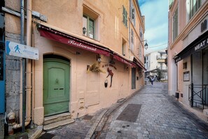 Eine schmale Kopfsteinpflasterstraße gesäumt von Gebäuden, darunter ein Restaurant mit roter Markise und ein Metzgerladen.