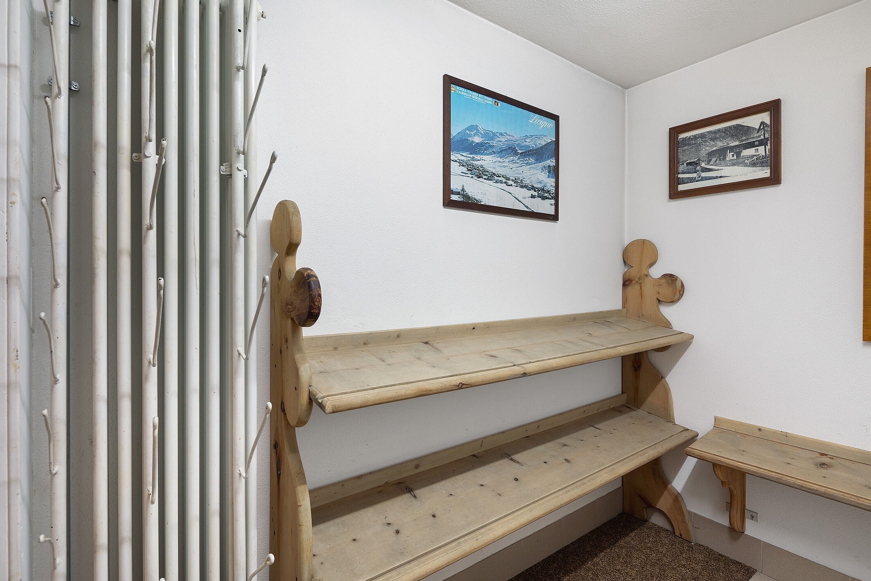 A corner with a wooden bench, a radiator, and two framed pictures on the wall.
