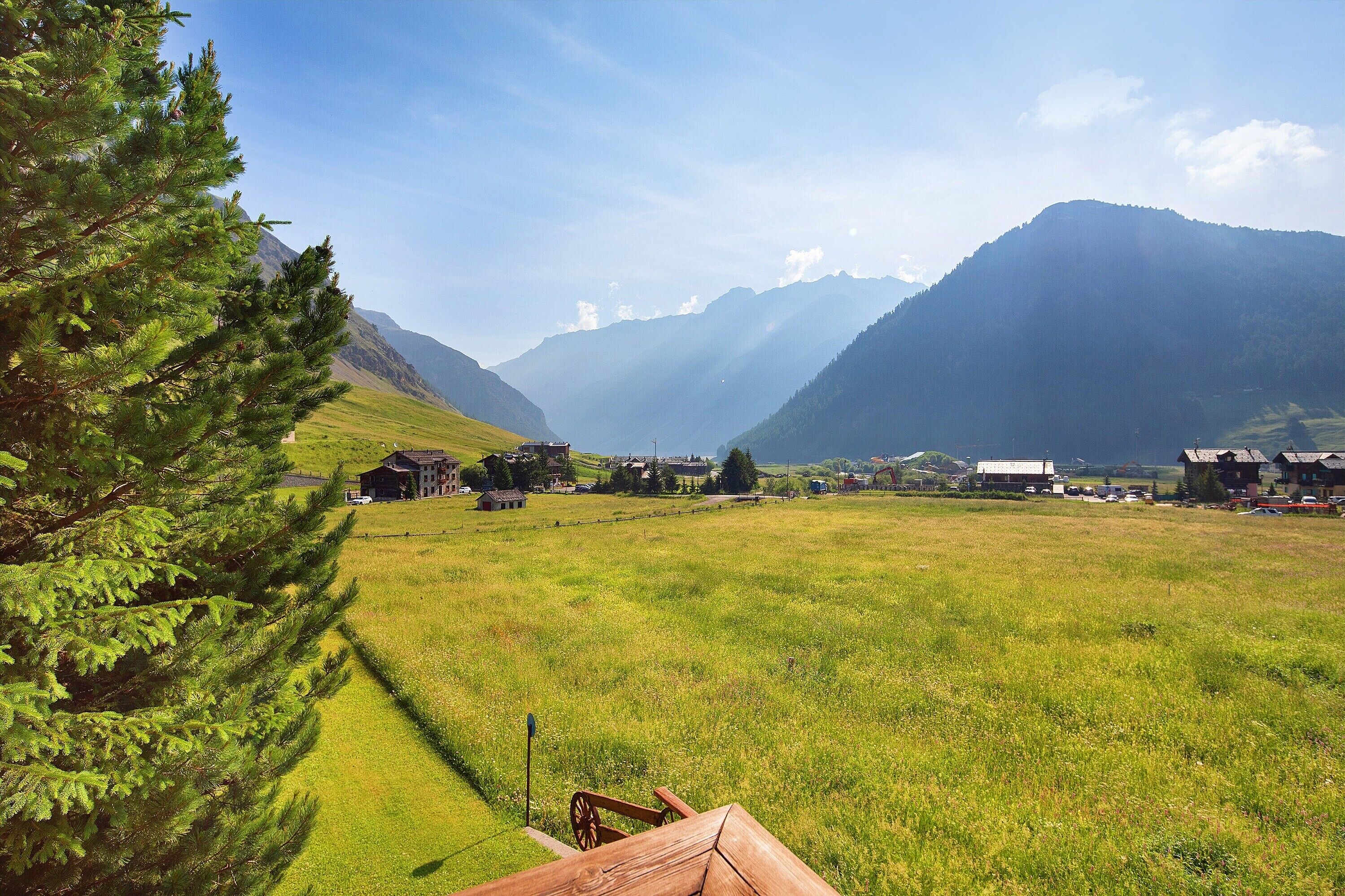 Paisaje rural con cielo despejado, una cordillera y un pequeño asentamiento con edificaciones.