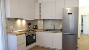 A modern kitchen with white cabinets, a stainless steel refrigerator, a built-in oven, and a wooden countertop. - Stay By Ilvesta Potam (Himarë)