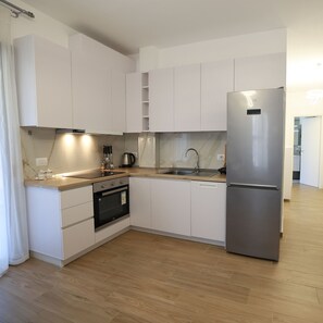 A modern kitchen with white cabinets, a stainless steel refrigerator, a built-in oven, and a wooden countertop. - Stay By Ilvesta Potam (Himarë)