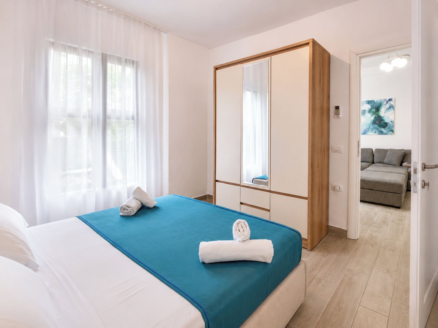 Une chambre d’hôtel comprenant un lit, une armoire, une salle de bain avec un miroir et donnant sur un canapé situé dans la pièce adjacente.