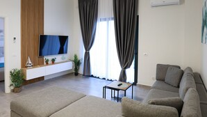 A modern living room with a flat-screen TV, a sofa, a coffee table, and a pendant light. - Stay By Ilvesta Potam (Himarë)