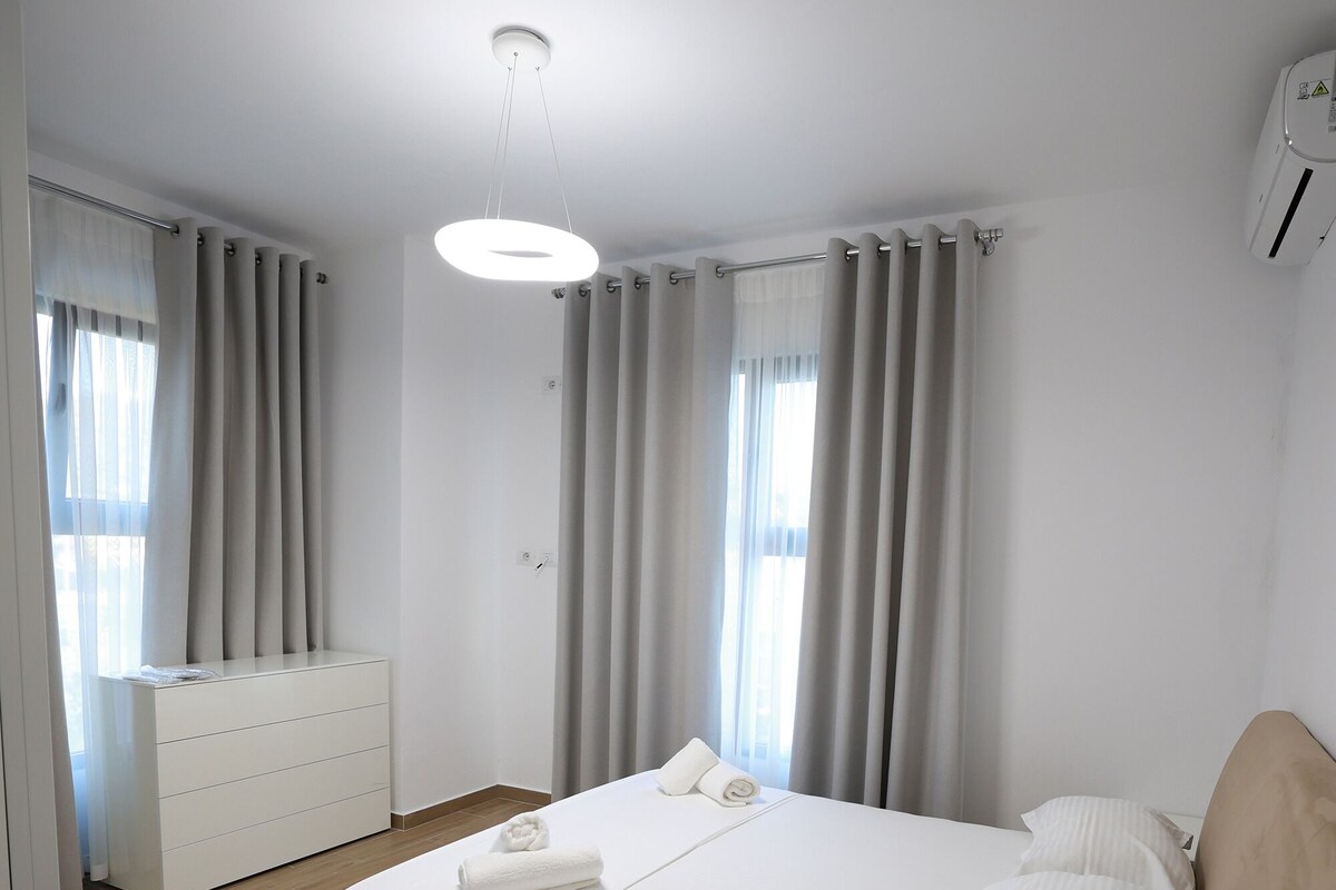 A modern bedroom with a bed, bedside tables, a dresser, and a ceiling light.