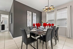 A dining area with a dark wall, modern chandelier, and a view of the outdoors through large windows. - 5Bd Villa Private Pool   Spa at Solara Resort 1820 (Kissimmee)