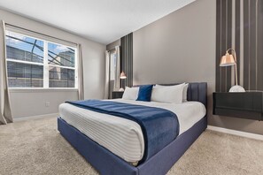A modern bedroom with a large bed, a window with blinds, a wall-mounted lamp, and a nightstand. - 5Bd Villa Private Pool   Spa at Solara Resort 1820 (Kissimmee)