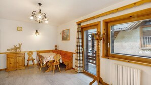A dining area with a wooden table, chairs, a chandelier, a clock, and a window with a view.