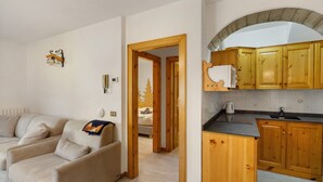 A living room with a sofa, a kitchen with wooden cabinets, and a doorway leading to another room.