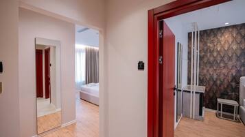 A hotel room with a wooden floor, a bed, a small table, and a red door.