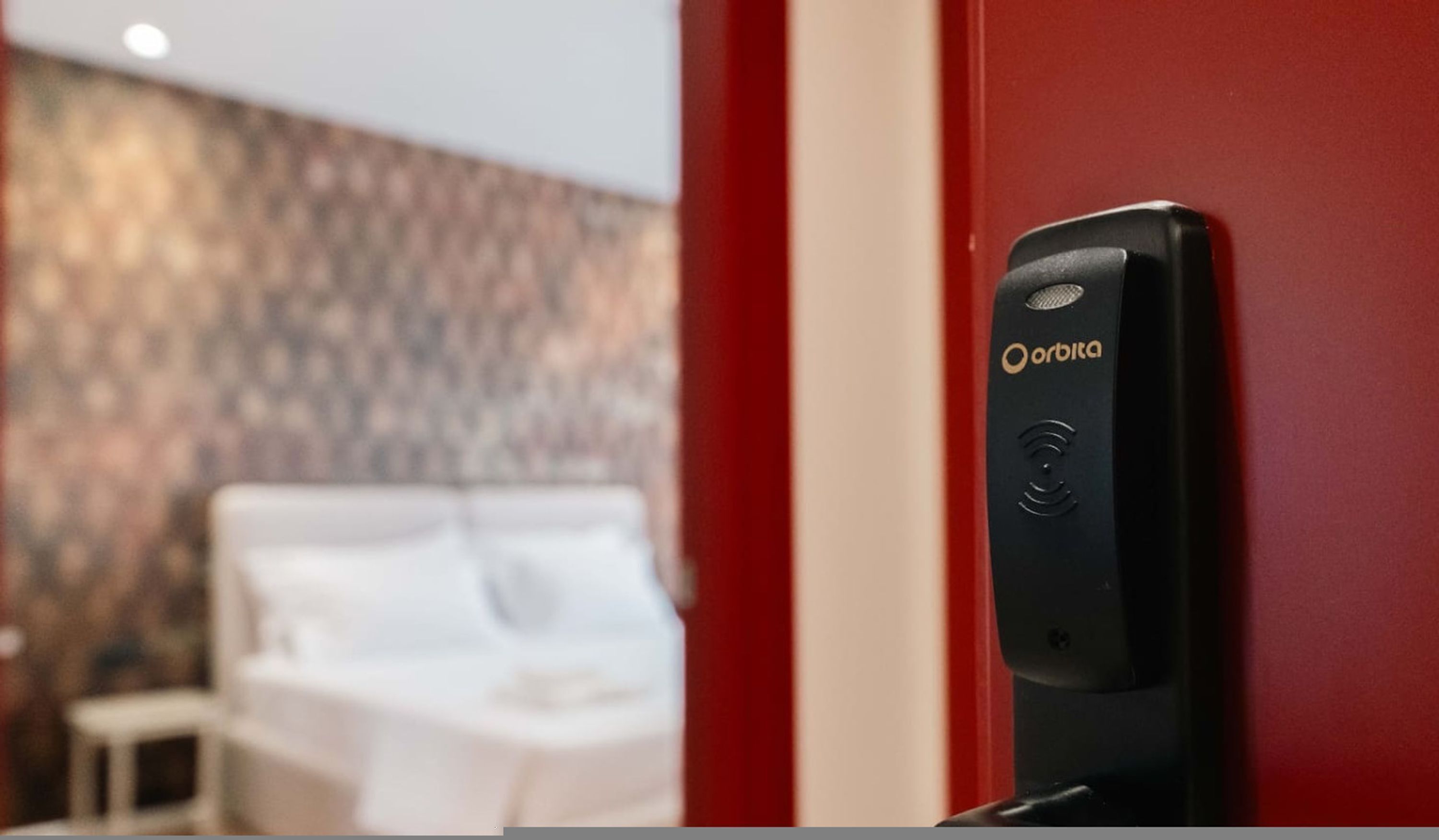 Une chambre d’hôtel avec un mur rouge et une porte sur laquelle est fixé un appareil « Orbita ».