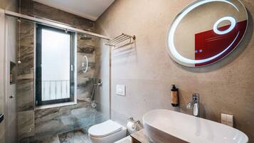 Een moderne badkamer met een douche met glazen wand, een groot ovaal wastafel en een ronde spiegel met een rode accentkleur.