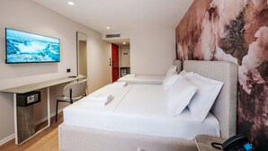 Une chambre d’hôtel avec un grand lit, un bureau avec un ordinateur, une télévision et un tableau au mur.