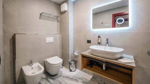 Une salle de bain moderne équipée d’un bidet, de toilettes et d’un grand miroir avec éclairage intégré.