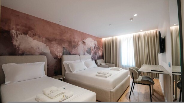 Une chambre d’hôtel avec deux lits, un bureau, une chaise et un téléviseur.