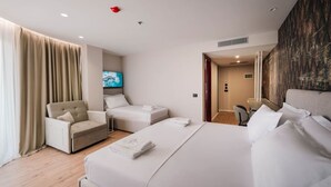 A modern hotel room with a large bed, a sofa, a desk, and a TV. - Ermes Deluxe Triple Room with Balcony and Sofa Bed (Durrës)