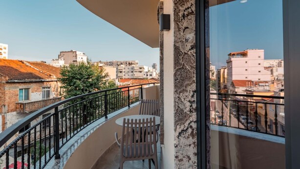 A balcony with a table and chairs, overlooking a cityscape with buildings and a clear sky. - Ermes Deluxe Triple Room with Balcony and Sofa Bed (Durrës)