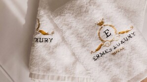 Two white towels with embroidered text and a crown symbol. - Ermes Deluxe Triple Room with Balcony and Sofa Bed (Durrës)