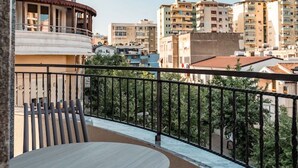 A balcony with a round table and chairs, overlooking a cityscape with multiple buildings. - Ermes Deluxe Triple Room with Balcony and Sofa Bed (Durrës)