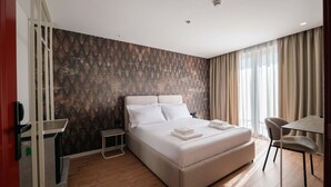 Ett modernt hotellrum med en stor säng, ett litet sängbord, en stol och ett skrivbord.
