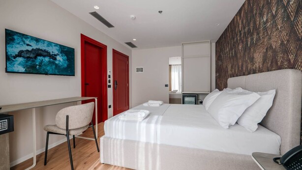 Ett modernt hotellrum med en säng, ett skrivbord, en stol och en TV.