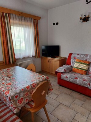 Une pièce comprenant une table à manger, un canapé, un téléviseur et une fenêtre avec des rideaux.