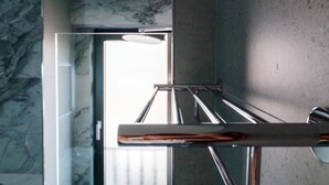 Moderni kylpyhuone, jossa on lasinen suihkuseinä, marmoriseinät ja näkyvillä oleva pyyheteline.