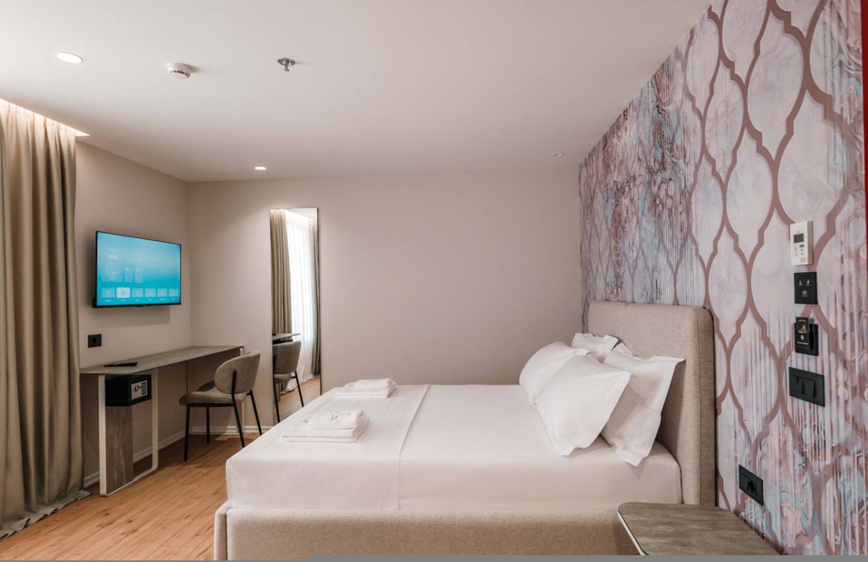 Une chambre d’hôtel avec un lit, un bureau, une chaise, une télévision et un mur décoré d’un motif.