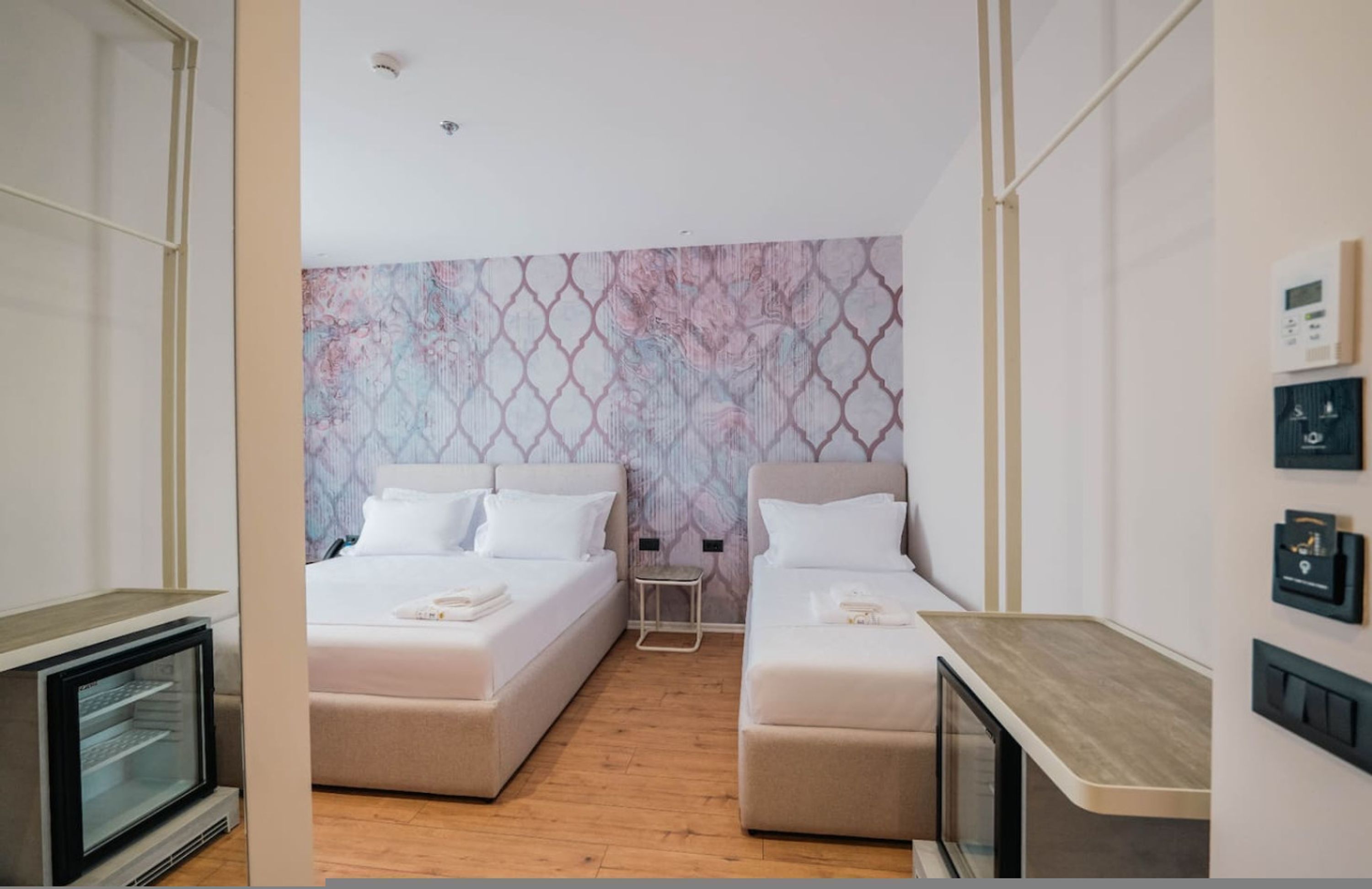 Una habitación de hotel moderna con dos camas, una mesita pequeña y televisor integrado.