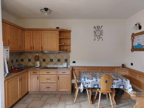 Une cuisine avec des meubles de rangement en bois, un pare-feu en carrelage, une table à manger avec des chaises et une horloge murale.