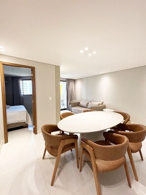 A modern dining area with a round table and six chairs, a sofa, and a bed in the adjacent room. - Vivere Resort By Day by Day (Cabedelo)