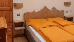 A bedroom with a wooden ceiling, a bed with orange bedding, a wooden wardrobe, and a cross on the wall.