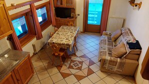 A compact living space with a dining table, wooden furniture, a sofa, and a television.
