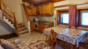 A kitchen with wooden cabinets, a dining table with a patterned tablecloth, a built-in oven, and a window with curtains.