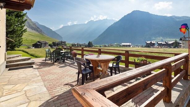 An outdoor seating area with stone flooring, wooden railings, and tables and chairs.