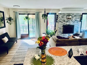 Un salon comprenant un canapé, une table basse ornée d’un vase de fleurs, une cheminée et une vue sur une piscine, visible à travers les portes vitrées.