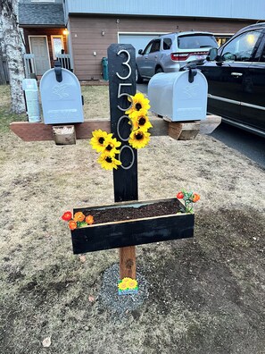 Een brievenbus met nummer 3500, omringd door zonnebloemen en een welkomstbord.