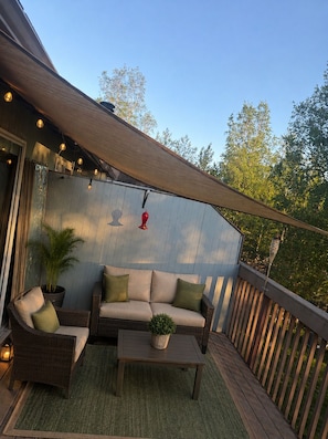An outdoor deck with a sofa, chairs, a table, and a potted plant.